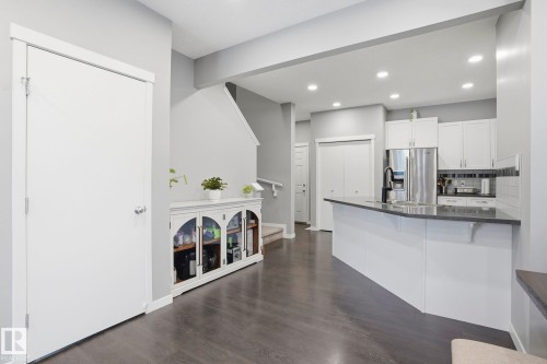 Open concept interior featuring dark wood-finish flooring, recessed lighting, a modern kitchen island with a dark countertop and sink, and white kitchen cabinetry with a tile backsplash - 4320 Annett Common, Edmonton, AB - Indoor Photo Showing Kitchen