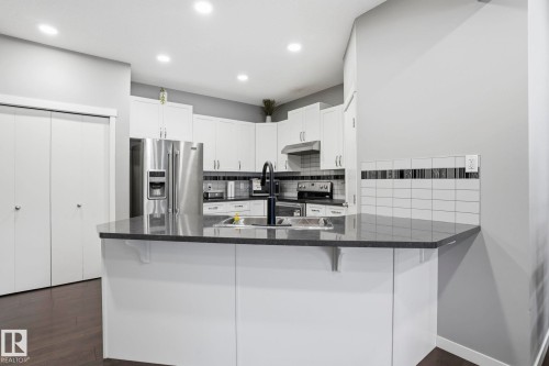 Kitchen featuring white cabinetry, dark countertops, stainless steel appliances, and a white subway tile backsplash with a decorative accent strip - 4320 Annett Common, Edmonton, AB - Indoor Photo Showing Kitchen With Upgraded Kitchen