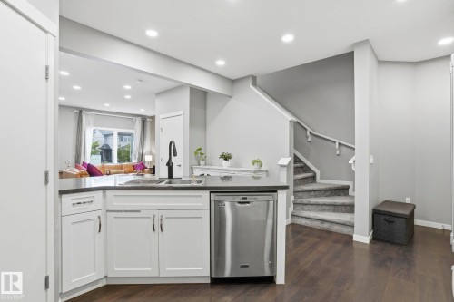 Kitchen island featuring white shaker cabinetry, an undermount sink with a gooseneck faucet, a stainless steel dishwasher, and a dark countertop - 4320 Annett Common, Edmonton, AB - Indoor