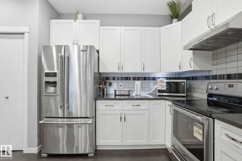 Modern kitchen featuring white shaker cabinetry, stainless steel appliances, dark countertops, and a subway tile backsplash with accent banding - 4320 Annett Common, Edmonton, AB - Indoor Photo Showing Kitchen