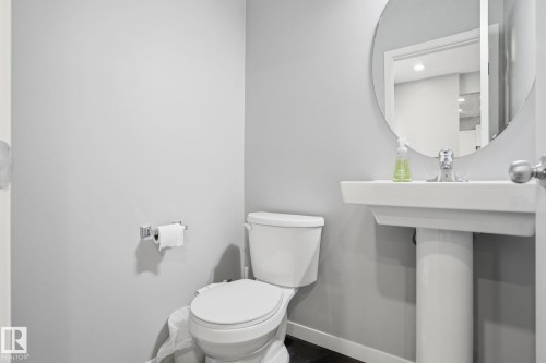 Bathroom featuring a white pedestal sink with a chrome faucet, a circular wall mirror, and a white toilet - 4320 Annett Common, Edmonton, AB - Indoor Photo Showing Bathroom