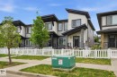 Modern townhome exterior featuring an asymmetrical roofline, light-toned vertical siding, dark grey horizontal siding, stone-clad columns, and a white picket fence - 4320 Annett Common, Edmonton, AB  - Outdoor 