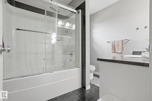 White bathtub with clear glass sliding shower doors and chrome fixtures - 4320 Annett Common, Edmonton, AB - Indoor Photo Showing Bathroom