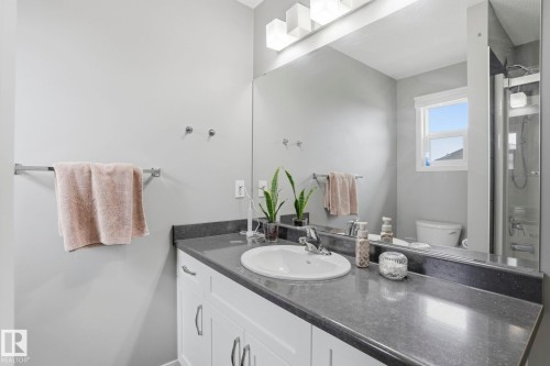 Bathroom vanity featuring a built-in sink, dark countertop, and white cabinetry with curved hardware - 4320 Annett Common, Edmonton, AB - Indoor Photo Showing Bathroom