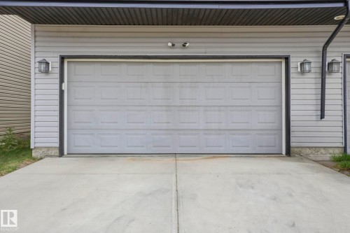 Exterior featuring a light grey paneled garage door, concrete driveway, and grey siding - 4320 Annett Common, Edmonton, AB - Outdoor With Exterior
