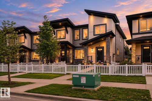 Modern townhome exterior featuring an asymmetrical roofline, mixed material facade with light siding and stone accents, and a white picket fence - 4320 Annett Common, Edmonton, AB - Outdoor
