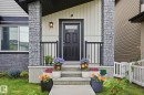 Welcoming front entry featuring a dark paneled door with glass insert, stone pillars, a concrete porch, black railings, and vertical siding - 4320 Annett Common, Edmonton, AB  - Outdoor With Exterior 