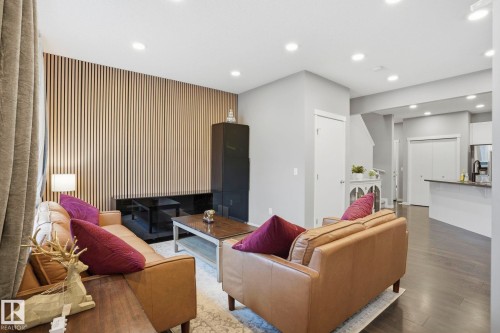 Living area featuring a slat wood accent wall with integrated dark-toned shelving, recessed lighting, and dark wood-finish flooring - 4320 Annett Common, Edmonton, AB - Indoor