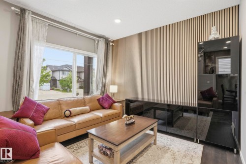 Living area featuring wood-finish flooring, a full-wall slatted wood-panel accent, and a large sliding glass door - 4320 Annett Common, Edmonton, AB - Indoor Photo Showing Living Room