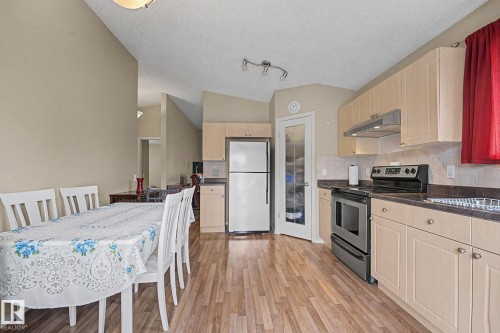 Kitchen and dining area featuring wood-finish flooring, light-toned cabinetry, stainless steel range, and a frosted glass pantry door - 19039 47 Avenue, Edmonton, AB 