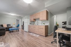 Open-concept living space featuring wood-finish flooring, a functional kitchenette with wood-tone cabinetry, a sink with a stainless steel faucet, and light-toned countertops - 