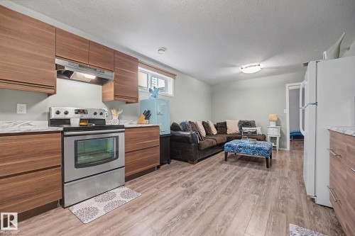 Open-concept living area featuring wood-finish flooring throughout, a stainless steel range with overhead ventilation, and contemporary wood-grain cabinetry - 19039 47 Avenue, Edmonton, AB 