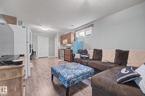 Open-concept living space featuring wood-finish flooring, a compact kitchen area with wood cabinetry, stainless steel appliances, and ample natural light from a horizontal window - 19039 47 Avenue, Edmonton, AB 
