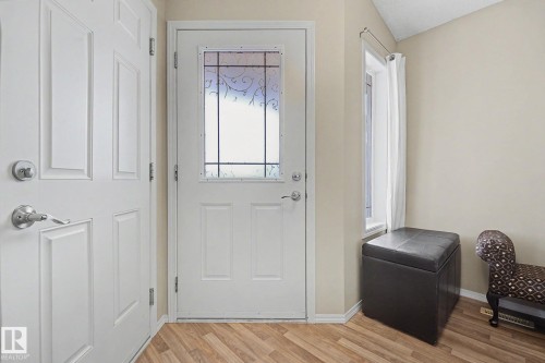 Entryway featuring a white paneled door with decorative glass insert, wood-finish flooring, a white paneled closet door, and a side window with white drapes - 19039 47 Avenue, Edmonton, AB 