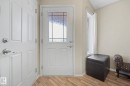 Entryway featuring a white paneled door with decorative glass insert, wood-finish flooring, a white paneled closet door, and a side window with white drapes - 19039 47 Avenue, Edmonton, AB 