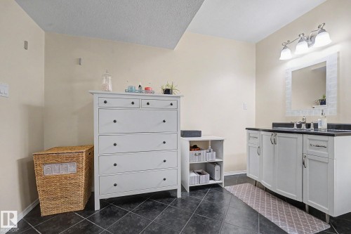 Bathroom featuring dark floor tiles and a vanity with white cabinetry, dark countertop, and a framed mirror - 19039 47 Avenue, Edmonton, AB 