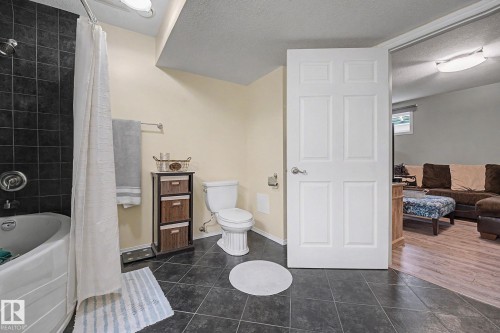 Bathroom featuring dark square floor tiles and a white bathtub with dark subway tile surround - 19039 47 Avenue, Edmonton, AB 