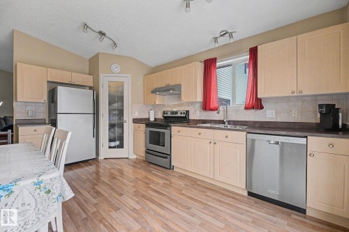 Kitchen featuring wood-finish flooring, ample cabinetry, stainless steel appliances, and a pantry with a glass-paneled door - 19039 47 Avenue, Edmonton, AB 