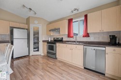 Kitchen featuring wood-finish flooring, light-toned cabinetry, stainless steel appliances, and track lighting - 