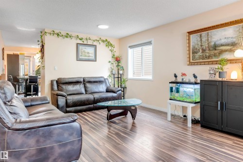 Open-concept living area featuring wood-finish flooring, a white-framed window with horizontal blinds, and a built-in ceiling light fixture - 312 Beringer Crescent, Edmonton, AB 
