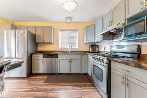 Well-appointed kitchen featuring wood-finish flooring, light gray cabinetry, and dark countertops - 312 Beringer Crescent, Edmonton, AB 