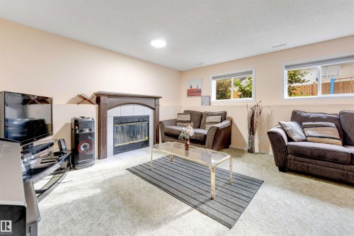 Living area featuring a dark wood mantel fireplace with a tiled surround, two windows, and light-colored carpeting - 312 Beringer Crescent, Edmonton, AB 