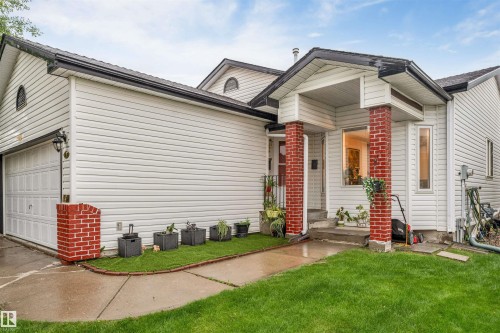 White siding exterior featuring a covered front entrance with brick pillars, an attached garage, and a manicured lawn - 312 Beringer Crescent, Edmonton, AB 