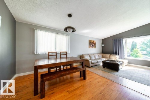 Open-concept living area featuring wood-finish flooring, a contemporary pendant light fixture, and a large window - 20 Chippewa Rd, Leduc, AB 