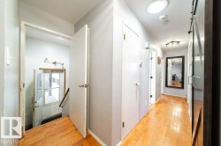 Hardwood flooring throughout a hallway featuring a circular ceiling light and a dark wood-finish barn door - 