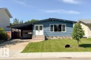 Blue siding exterior featuring white double entry doors, stone veneer foundation, and a carport leading to a garage - 20 Chippewa Rd, Leduc, AB 