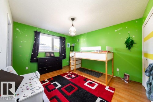 Room featuring wood-finish flooring, a double window with dark curtains, and a ceiling-mounted pendant light fixture - 20 Chippewa Rd, Leduc, AB 