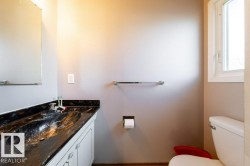 Bathroom featuring a single vanity with a dark, patterned countertop and integrated sink, white cabinetry with decorative pulls, and a wall-mounted mirror - 