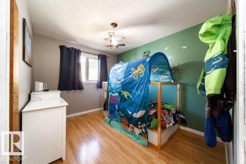 Bedroom featuring wood-finish flooring, a window with dark curtains, and a ceiling fan with a light fixture - 20 Chippewa Rd, Leduc, AB 