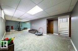 Spacious lower-level area featuring a drop ceiling with integrated lighting, a mix of carpet and wood-finish flooring, and a staircase with white risers - 