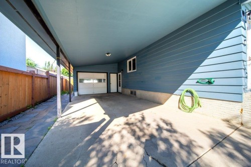 Carport featuring concrete flooring, a side entrance, and a garage door with clear panels - 20 Chippewa Rd, Leduc, AB 