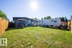 Expansive grassy yard area with a wood privacy fence and a blue-sided dwelling featuring a patio with a gazebo - 