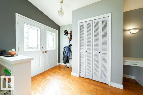 Entryway featuring double doors with decorative glass panels, wood-finish flooring, a built-in closet with louvered bifold doors, and a built-in desk area with a wall sconce - 20 Chippewa Rd, Leduc, AB 