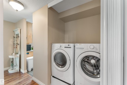 Dedicated laundry area featuring a stacked front-load washer and dryer set, neutral wall paint, and wood-finish flooring - 5802 172 Street, Edmonton, AB 