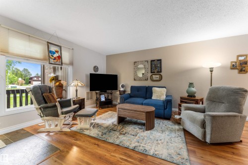 Inviting living space featuring wood-finish flooring, a neutral wall palette, and a large window providing outdoor scenery - 5802 172 Street, Edmonton, AB 