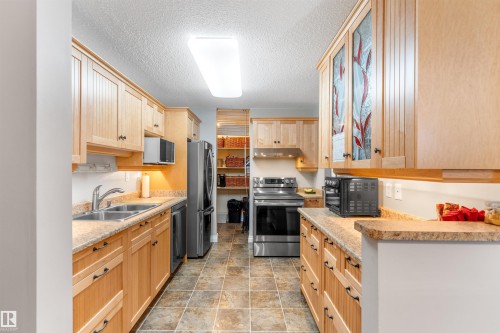 Galley kitchen featuring light wood cabinetry with varied panel designs, stainless steel appliances, and durable tiled flooring - 5802 172 Street, Edmonton, AB 