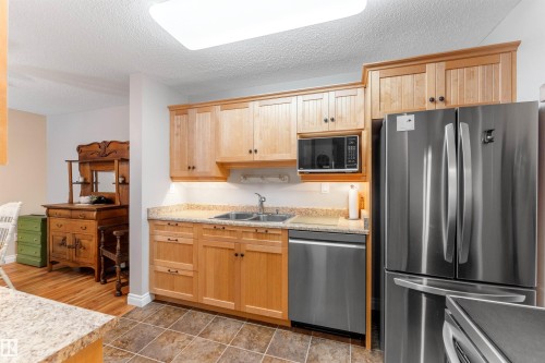 Kitchen featuring natural wood cabinetry, light-toned countertops, stainless steel appliances, and tiled flooring - 5802 172 Street, Edmonton, AB 