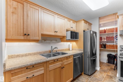Kitchen featuring wood cabinetry, a double basin stainless steel sink, a stainless steel refrigerator, and a built-in microwave - 5802 172 Street, Edmonton, AB 