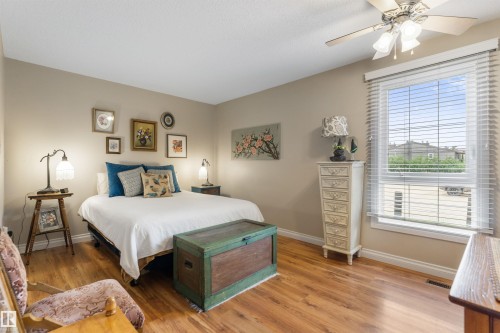 Bedroom featuring wood-finish flooring, a ceiling fan with integrated lighting, and a large window with horizontal blinds - 5802 172 Street, Edmonton, AB 