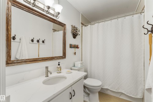 Bathroom featuring a vanity with a white countertop and undermount sink, brushed nickel faucet, and a large framed mirror - 5802 172 Street, Edmonton, AB 