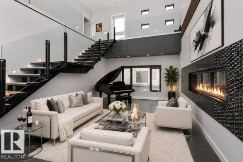 Open-concept living area featuring a linear fireplace with a mosaic tile surround, a floating staircase with glass railings and wood-finish treads, and dark tile flooring - 9035 Saskatchewan Drive, Edmonton, AB 