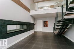 Two-story space featuring a linear fireplace with dark tile surround, a floating spiral staircase with glass railing, an upper-level glass railing, wood-finish wall accents, and large format floor tile - 