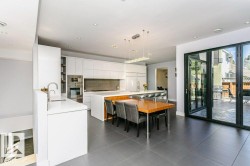 Open-concept kitchen featuring white cabinetry, integrated appliances, a central island with countertop seating, recessed lighting, and large accordion-style glass doors opening to the exterior - 