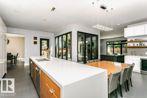 Modern kitchen featuring a large white countertop island with integrated sink, wood-finish cabinetry, and stainless steel appliances - 9035 Saskatchewan Drive, Edmonton, AB 