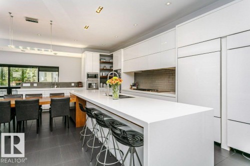 Contemporary kitchen with a large central island, integrated panel-ready appliances, white cabinetry, a subway tile backsplash, and dark tile flooring - 9035 Saskatchewan Drive, Edmonton, AB 