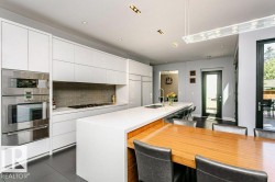 Modern kitchen featuring white flat-panel cabinetry, integrated stainless steel appliances, a waterfall island, and a gray subway tile backsplash - 
